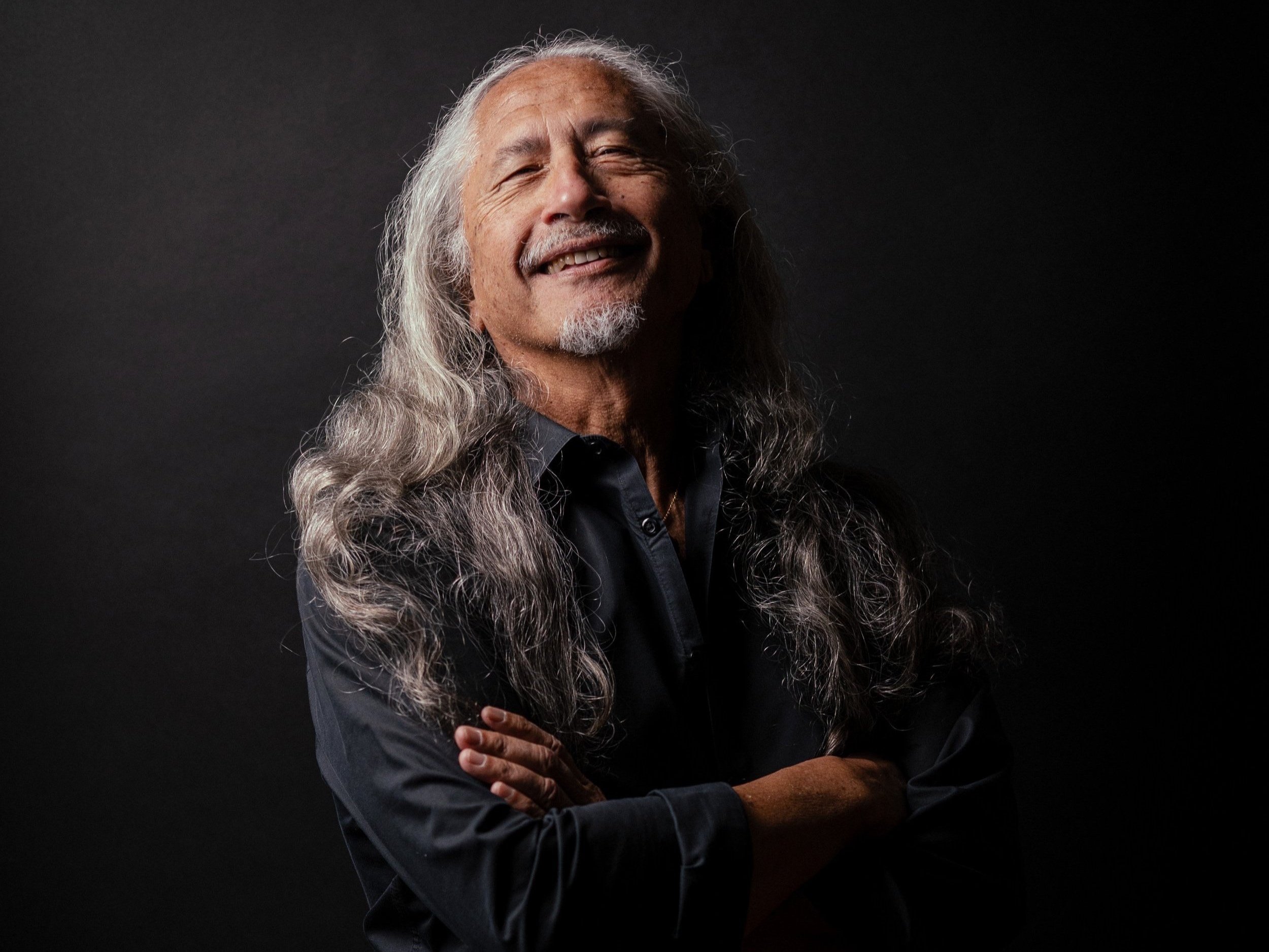Smiling older man with long gray hair and beard against a dark background